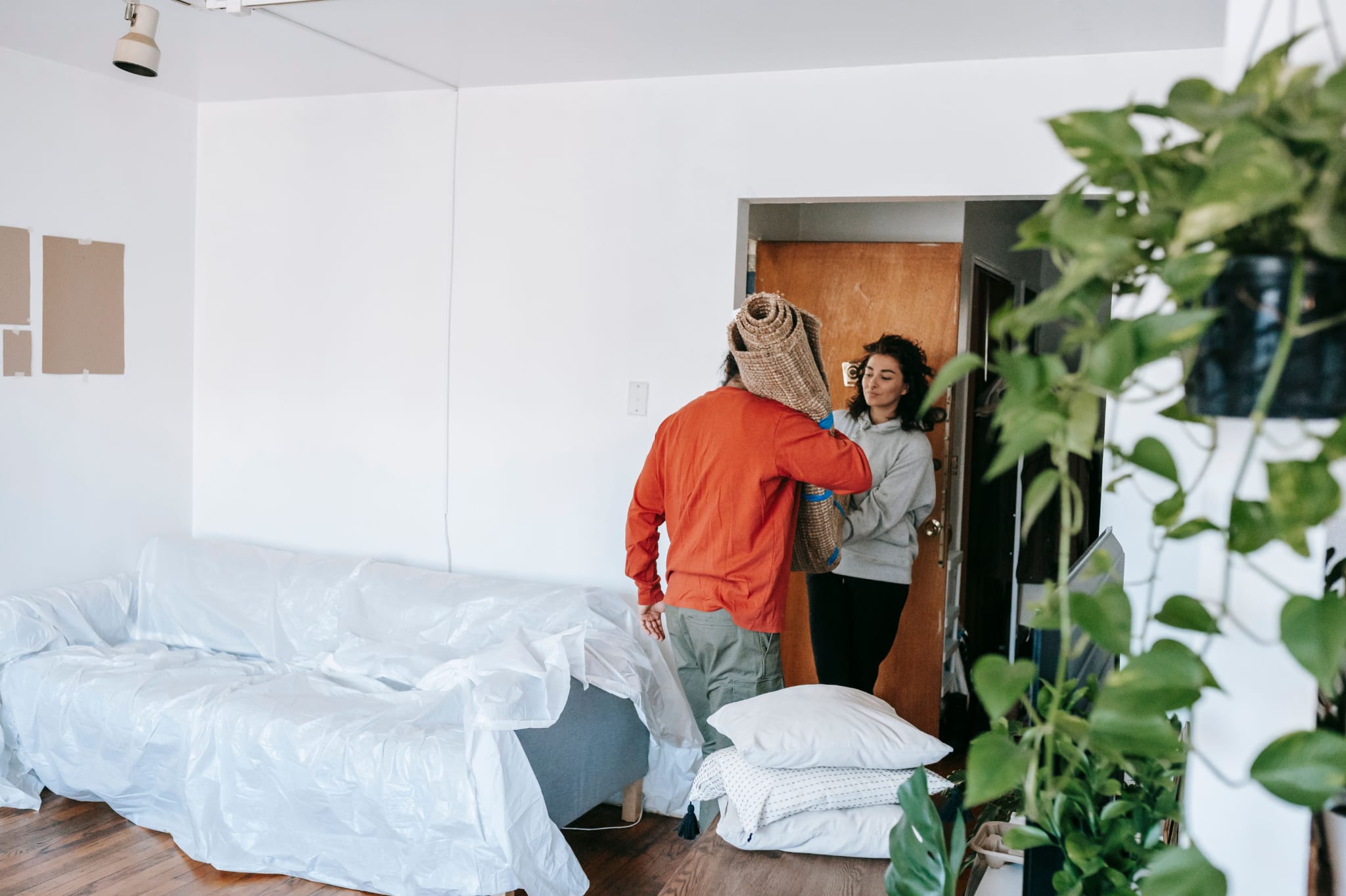 Two people carrying a rolled rug through a doorway while moving items out of a property